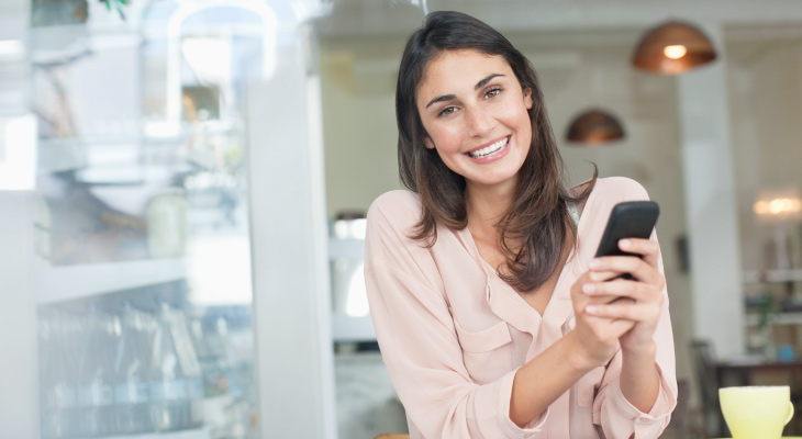 brunette woman sitting in coffee shop smiling holding her phone