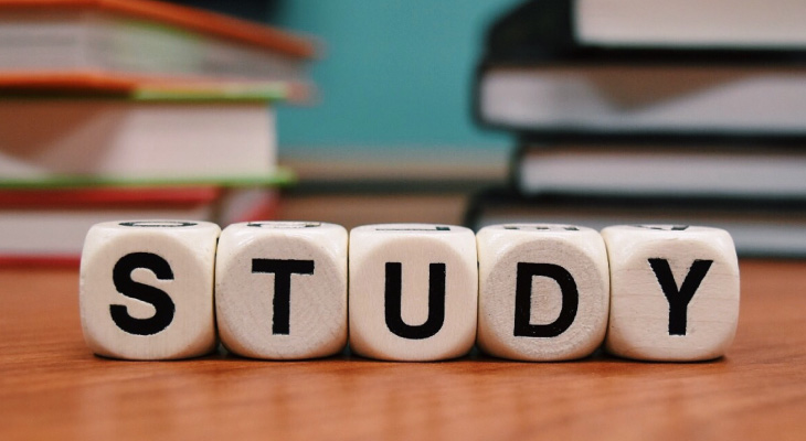 Five Boggle letter cubes spell STUDY on a wooden table against a background of two stacks of books