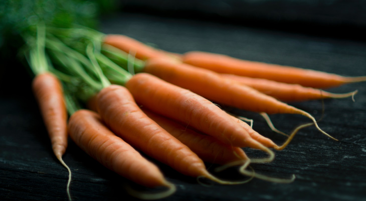 Cluster of orange carrots with green stems that promote saliva production when eaten