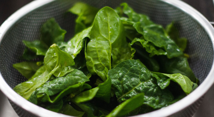 Closeup of silver colander filled with leafy greens that support healthy teeth