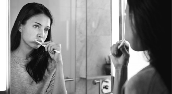young woman brushing her teeth in front of the bathroom mirror