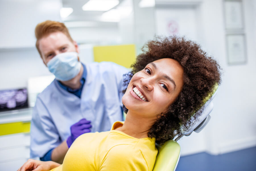 Curly haired woman in a yellow shirt smiles while sitting in the dental chair at the dentist in Tampa, FL