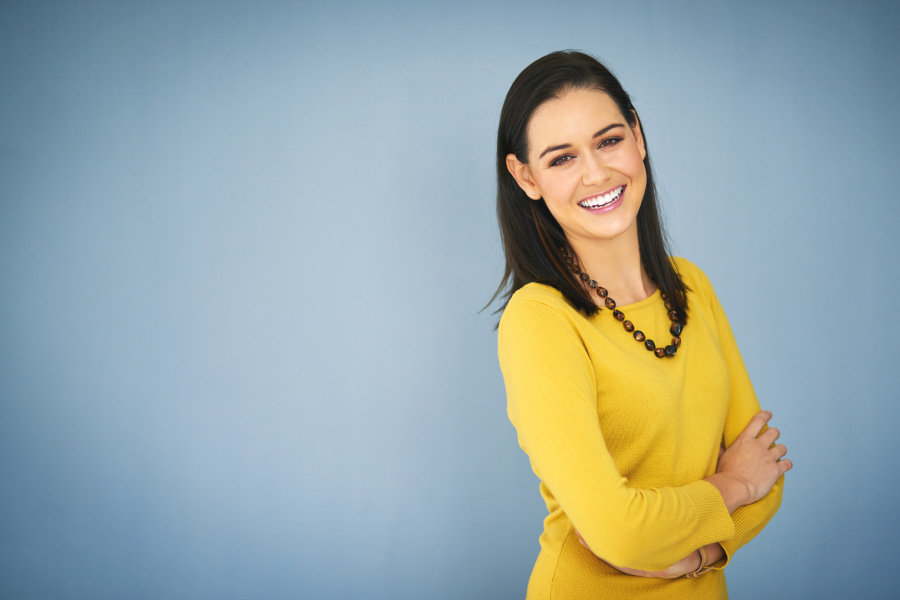 Brunette woman smiles after a smile makeover with veneers in Temple Terrace, FL, in a yellow blouse